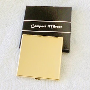 以下が含まれることがあります： 金色の正方形のコンパクトミラーで、それに合わせた金色の仕上げが施されています。 コンパクトは、白いスクリプトで「Compact Mirror」と書かれた黒い箱の隣にあります。 箱は白いバンドで包まれています。