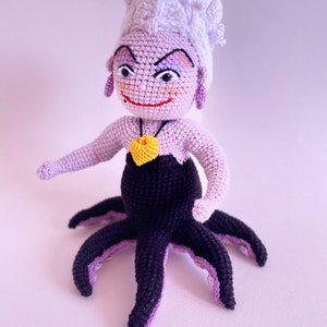 May include: A crocheted Ursula doll from The Little Mermaid. She has purple skin, a white crocheted crown, and a black crocheted octopus tail.