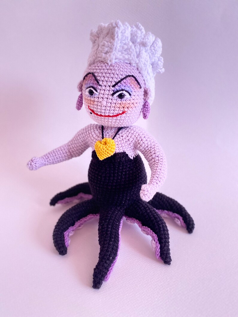 May include: A crocheted Ursula doll from The Little Mermaid. She has purple skin, a white crocheted crown, and a black crocheted octopus tail.