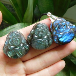 Puede incluir: Tres colgantes de piedra de labradorita tallados en forma de Buda sonriente. Los colgantes son de color azul verdoso oscuro con destellos iridiscentes de azul y verde.