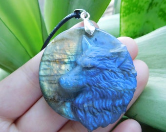 Könnte beinhalten: Ein runder Labradorit-Anhänger in Blau und Gold mit einem geschnitzten Wolfskopf-Design. Der Anhänger ist an einer schwarzen Schnur.