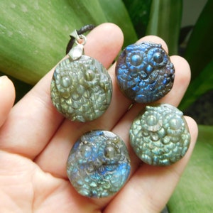 Op de afbeelding: Drie ronde labradorite uil hangers met iriserende blauwe en groene kleuren. De hanger links is aan een zwart koord met een zilveren sluiting.
