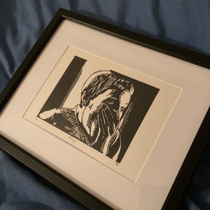 May include: Black and white framed print of a person with their face in their hands. The print is titled "Dreaming" and is signed by the artist.