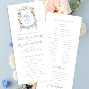 May include: Two white wedding program cards with blue text and a watercolor floral crest featuring the initials JG. The front card lists the couple's names, Julia Marie Fletcher and George James Collins, the date June 22, 2027, and the ceremony order.