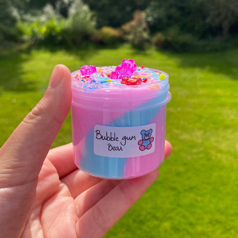 May include: A clear plastic jar filled with pink and blue slime with colorful sprinkles and gummy bears on top. The jar has a white label that says "Bubble gum Bear".
