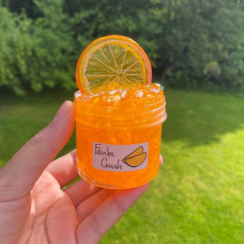 May include: Orange-scented slime in a clear jar with a label that says "Fanta Gush" and an orange slice on top.