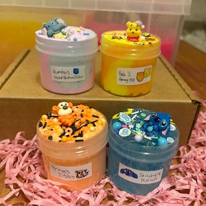 May include: Four small jars of slime with different colors and toppings. The slime is labeled with names like "Dumbo's Marshmallow", "Pooh's Honey Pot", "Springy Tiggy", and "Stitch's Ocean".