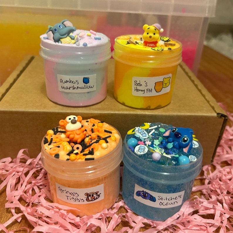May include: Four small jars of slime with different colors and toppings. The slime is labeled with names like "Dumbo's Marshmallow", "Pooh's Honey Pot", "Springy Tiggy", and "Stitch's Ocean".