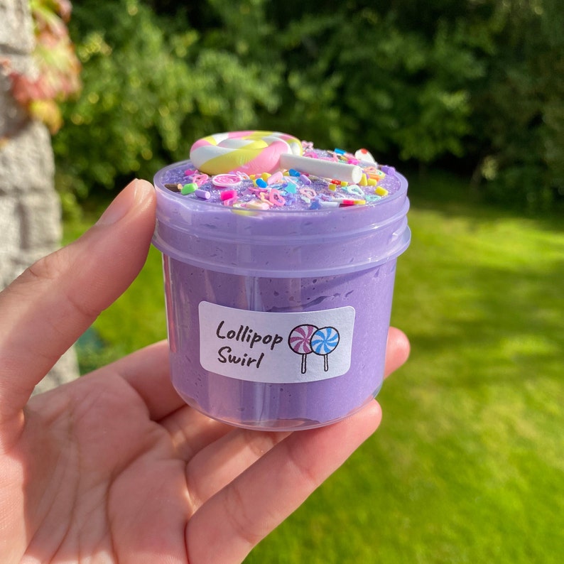 May include: Purple slime in a clear jar with a label that says "Lollipop Swirl". The slime is topped with colorful sprinkles and a pink and yellow lollipop.