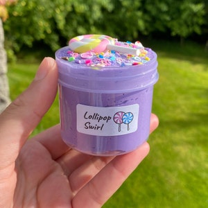 May include: Purple slime with sprinkles and a lollipop on top in a clear jar with a label that says "Lollipop Swirl"
