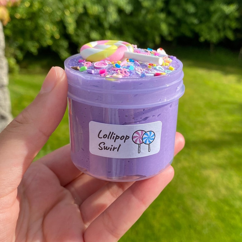 May include: Purple slime with sprinkles and a lollipop on top in a clear jar with a label that says "Lollipop Swirl"
