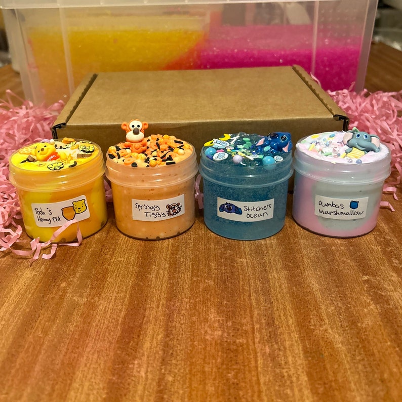 May include: Four small jars of slime with different colors and textures. The jars are labeled with names like "Pooh's Honey Pot", "Springy Tiggy", "Stitch's Ocean", and "Dumbo's Marshmallow".