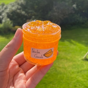 May include: Orange slime in a clear jar with a label that says "Fanta Crush" and a picture of an orange slice.