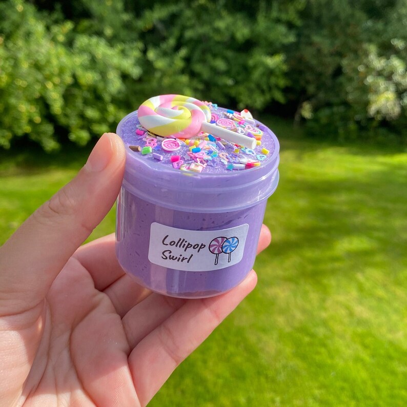 May include: Purple slime with sprinkles and a lollipop on top in a clear jar with a label that says "Lollipop Swirl"