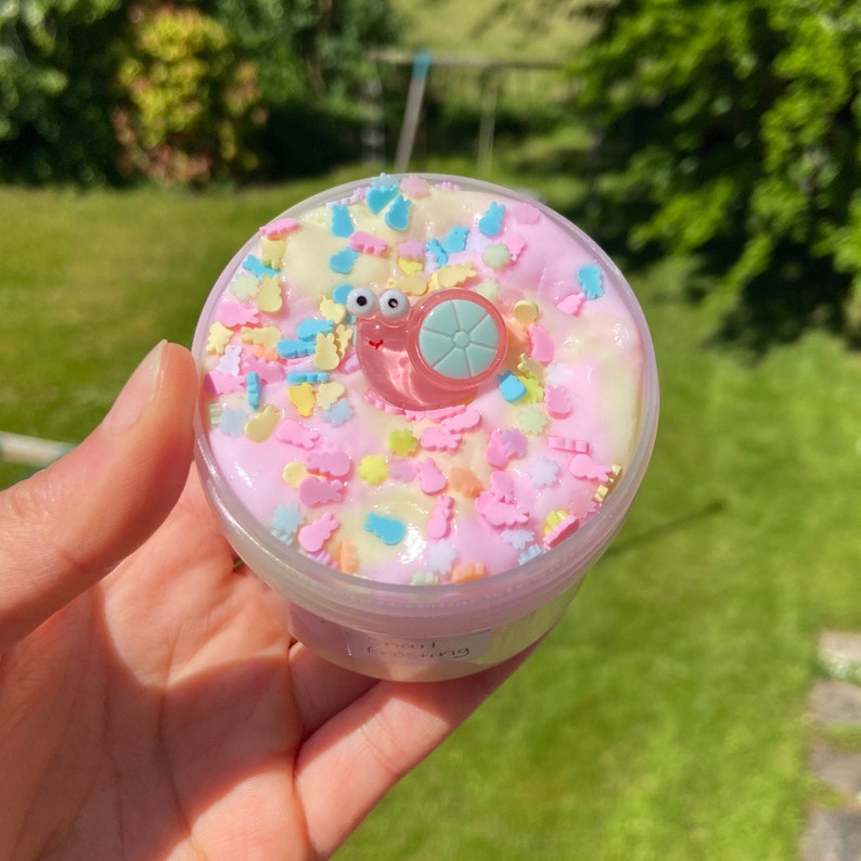 May include: A clear plastic container filled with pink slime with colorful sprinkles and a small pink snail charm.