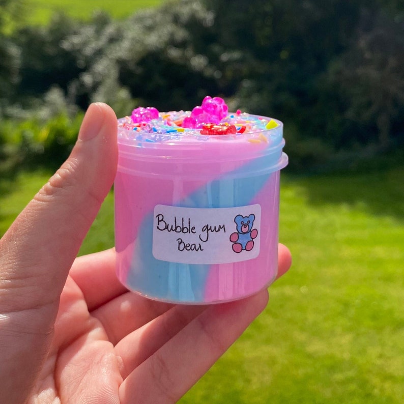May include: A small clear jar filled with pink and blue slime with colorful sprinkles and gummy bears on top. The jar has a white label that says "Bubble gum Bear".