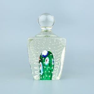 May include: Clear glass bottle with a rounded stopper. The bottle features a green cactus design with white, red, and blue floral accents. The glass is filled with tiny bubbles, adding a decorative touch.