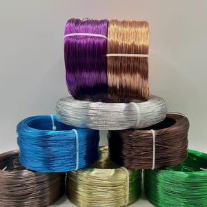 May include: A collection of colorful spools of wire in various shades, including purple, copper, silver, blue, brown, gold, and green. Each spool is neatly wound and secured with a white band, showcasing a range of crafting supplies.