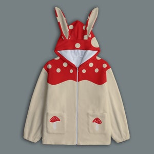 May include: A cream-colored hooded jacket with red mushroom-shaped ears and red and white polka dots on the hood. The jacket has a zipper closure and two pockets with red mushroom appliques.