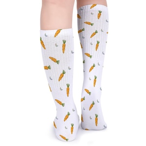May include: White knee-high socks with a repeating pattern of orange carrots and small gray crescent moons. The socks are made of a soft, ribbed material.