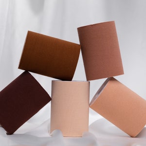 Puede incluir: Cinco rollos de cinta de doble cara en diferentes tonos de marrón, beige y marrón claro. Los rollos están apilados uno encima del otro.