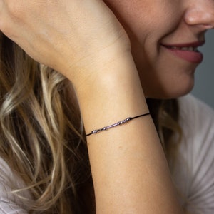 May include: A simple black string bracelet with silver beads and a silver bar charm.