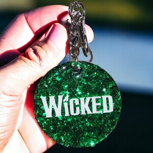 May include: A green glitter keychain with the word "WICKED" in white letters.