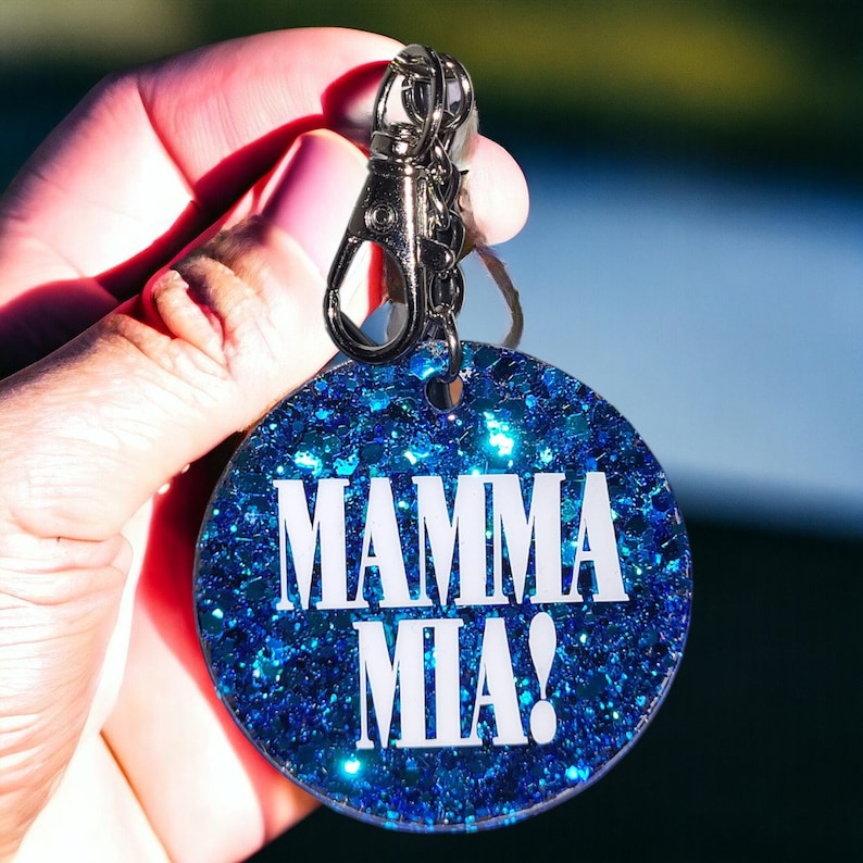 May include: A blue glitter keychain with a silver key ring and the text "Mamma Mia!" in white.