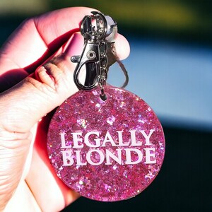 May include: Pink glitter keychain with the text "LEGALLY BLONDE" in white lettering.