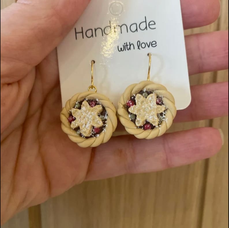 May include: A pair of gold dangle earrings with a brown and white pie design. The pie has a white star in the center and pink and green sprinkles around the edge. The earrings are handmade with love.