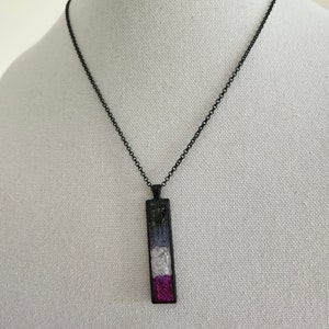 May include: A black chain necklace with a rectangular pendant featuring a mosaic of black, gray, white, purple, and pink glass pieces.