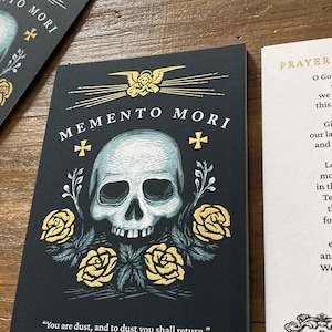 Op de afbeelding: Memento Mori print met een zwarte achtergrond, een witte schedel met een gouden kruis erboven en drie gouden rozen met groene bladeren. De tekst "You are dust, and to dust you shall return" staat onderaan de print.