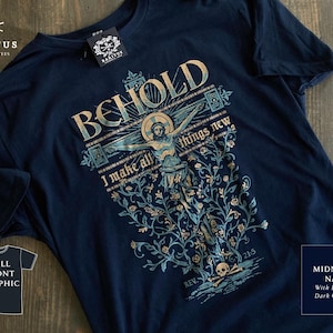 Puede incluir: Camiseta azul marino medianoche con un gráfico que presenta el texto "BEHOLD I make all things new" y una representación de Jesús en la cruz. El diseño incluye tinta azul y dorada oscura. La camiseta tiene una etiqueta que dice "BARITUS CATHOLIC TEES".
