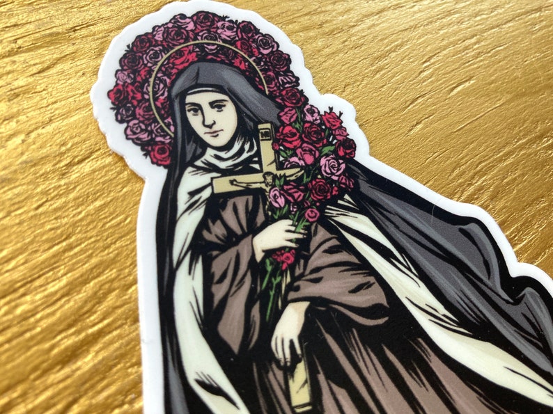 May include: A sticker featuring a saintly figure with a halo of pink roses, holding a bouquet of roses and a cross. The figure is dressed in a black veil and brown robes, with a white undergarment. The sticker has a white border.