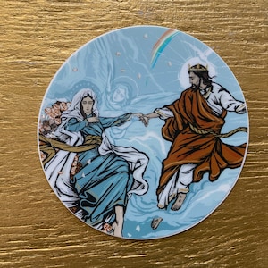 May include: Round sticker featuring a religious illustration. The artwork depicts two figures, one in a blue robe and the other in a brown robe, reaching for each other. A rainbow and clouds are in the background. The sticker is on a gold surface.