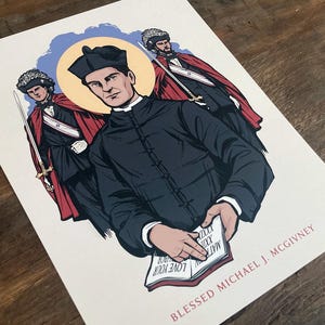 Può includere: Una stampa rettangolare con un'illustrazione centrale del beato Michael J. McGivney in tonaca nera con un'aureola gialla, affiancato da due figure con mantelli rossi e cappelli piumati che impugnano spade. Il testo recita BLESSED MICHAEL J. MCGIVNEY.