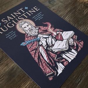 May include: A dark blue print featuring Saint Augustine, with text that reads "SAINT AUGUSTINE" and "You have made us for yourself, O Lord." The illustration depicts Saint Augustine holding a book and quill.