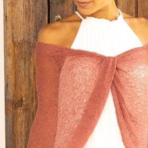 May include: A dusty rose knitted shawl draped over a person's shoulders. The shawl is made of a lightweight, open-weave fabric.