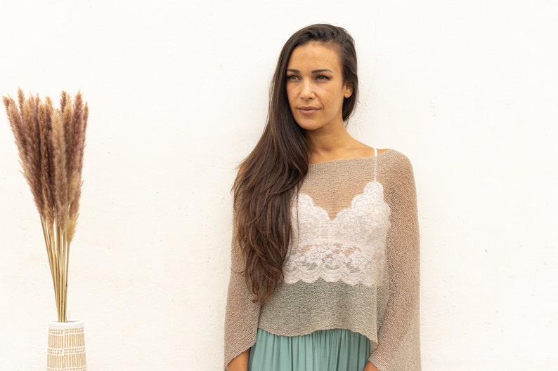 May include: A woman with long brown hair wearing a light brown sheer top over a white lace crop top and a teal green skirt.
