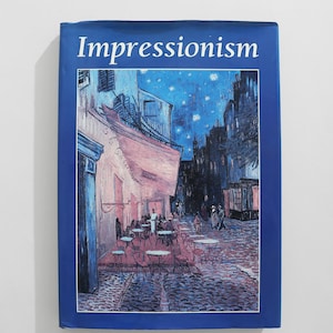May include: A book titled "Impressionism" with a blue cover. The cover features a painting of a street scene at night, with a cafe and people. The painting is in shades of blue, pink, and white.