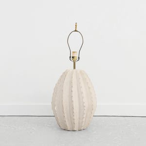 May include: A white ceramic table lamp shaped like a cactus with a gold metal base and a black wire lampshade.