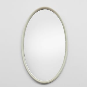 May include: Oval-shaped mirror with a pale green frame. The mirror is centered against a white background, creating a minimalist aesthetic. The frame has a smooth, matte finish. The mirror's reflective surface is clear and clean.