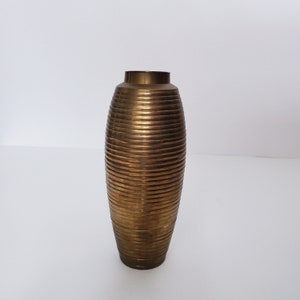 May include: A gold metal vase with a ribbed design. The vase is oval shaped and has a smooth, polished finish.