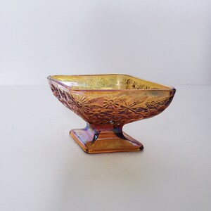 May include: A vintage amber glass candy dish with a floral design. The dish has a square base and a rounded bowl.