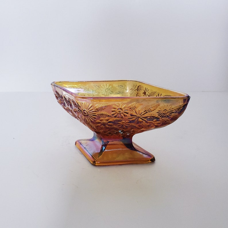May include: A vintage amber glass candy dish with a floral design. The dish has a square base and a rounded bowl.