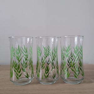 Könnte beinhalten: Drei transparente Gläser mit einem grünen Bambusblatt-Design. Die Gläser sind zylindrisch mit einem leicht ausgestellten Boden. Das Bambusmuster ist in einem leuchtenden Grün gemalt und erzeugt eine natürliche und erfrischende Ästhetik.