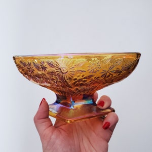 May include: A vintage iridescent amber glass bowl with a floral design. The bowl has a pedestal base and is perfect for serving snacks or desserts.