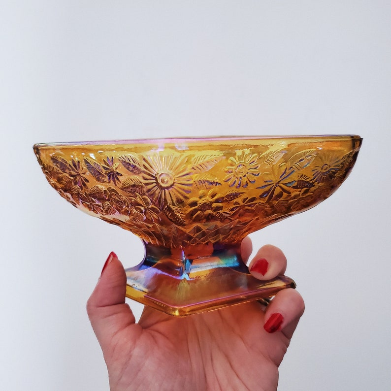 May include: A vintage iridescent amber glass bowl with a floral design. The bowl has a pedestal base and is perfect for serving snacks or desserts.