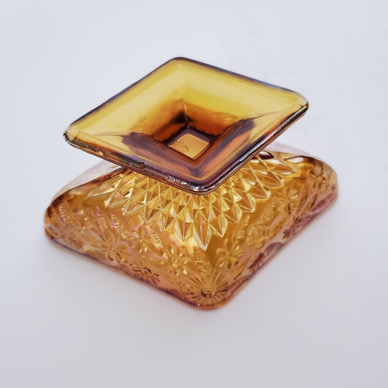 May include: A square amber glass dish with a raised, square center. The dish has a diamond pattern and floral design.