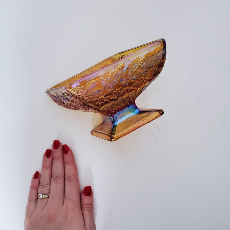 May include: A vintage iridescent amber glass candy dish with a floral design. The dish has a pedestal base and is perfect for serving candy, nuts, or other small treats.